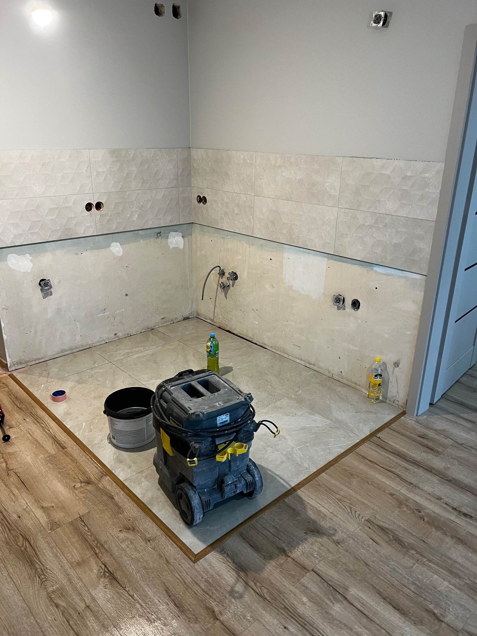 Wnętrze łazienki w trakcie wykończenia: położone płytki na podłodze i częściowo na ścianach, widoczny odkurzacz przemysłowy i akcesoria.