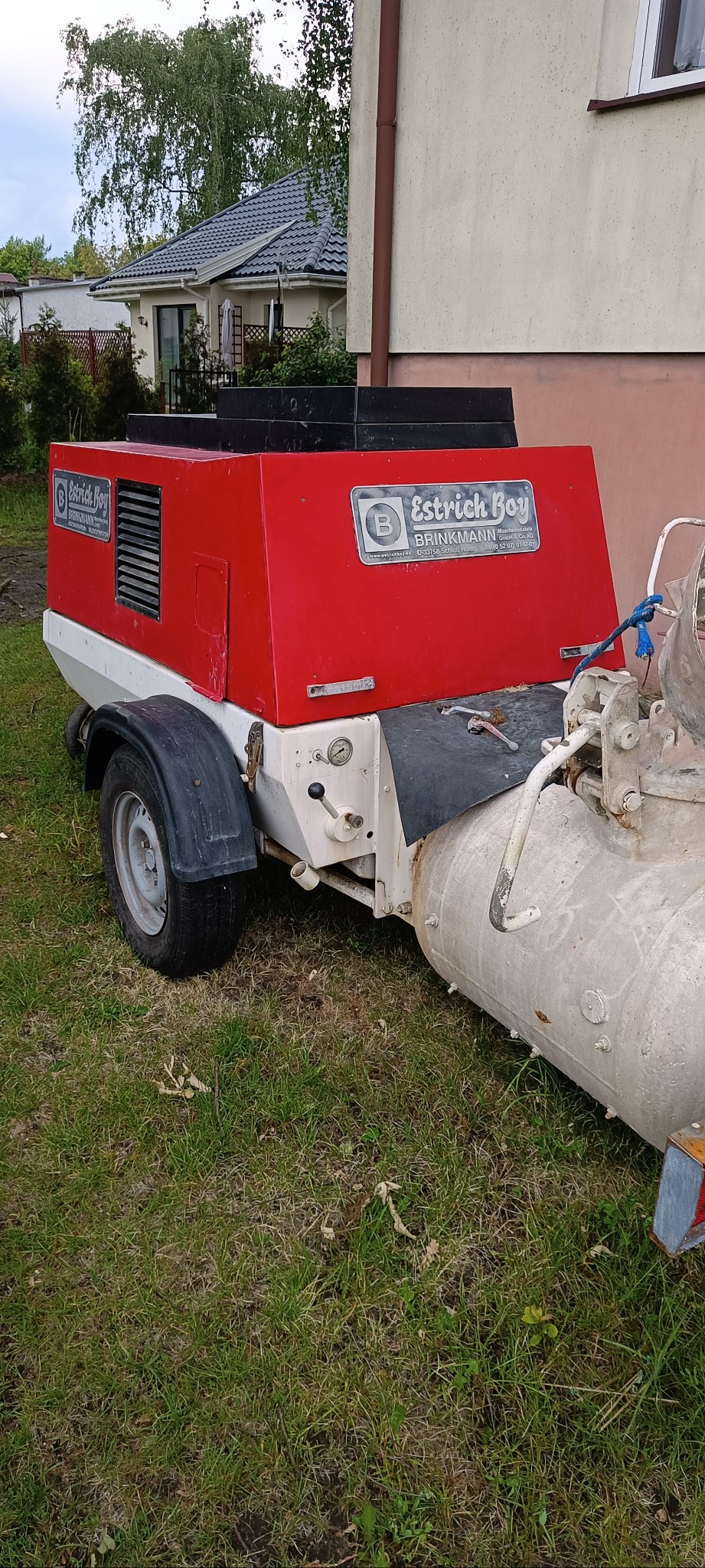 Agregat do posadzek jastrychowych marki Brinkmann, model Estrich Boy, stojący na trawie. Widoczny fragment budynku w tle. Sprzęt z widocznymi śladami użytkowania.