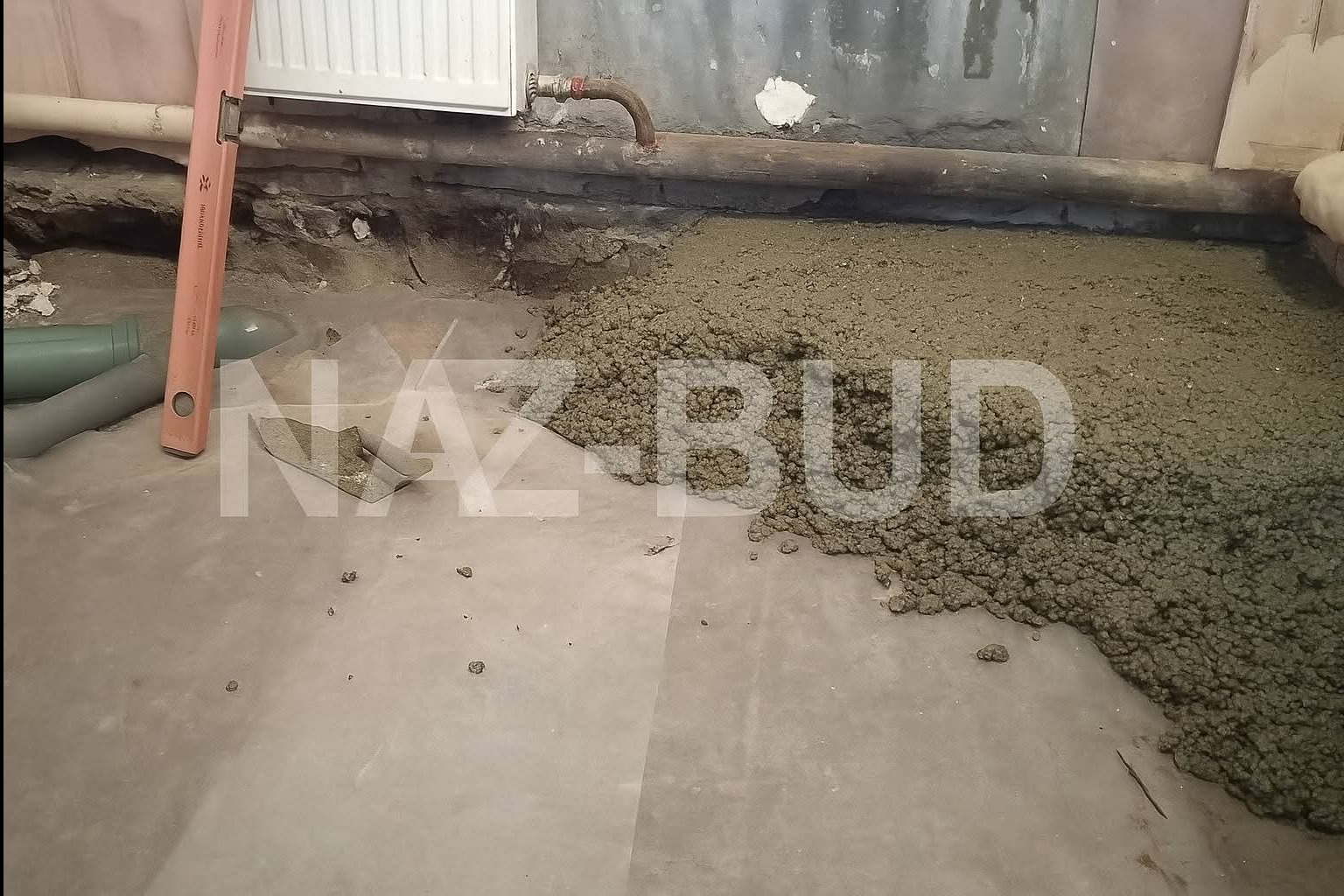 Wylewka jastrychowa na folii, z widocznym poziomem i fragmentem grzejnika. Częściowo rozprowadzona masa, surowy stan, przygotowanie do dalszych prac wykończeniowych.