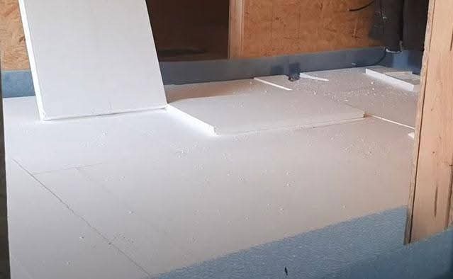 Białe płyty styropianowe ułożone na podłożu z niebieską izolacją, przygotowane pod wylewkę jastrychową. Widoczne fragmenty ścian i instalacji.