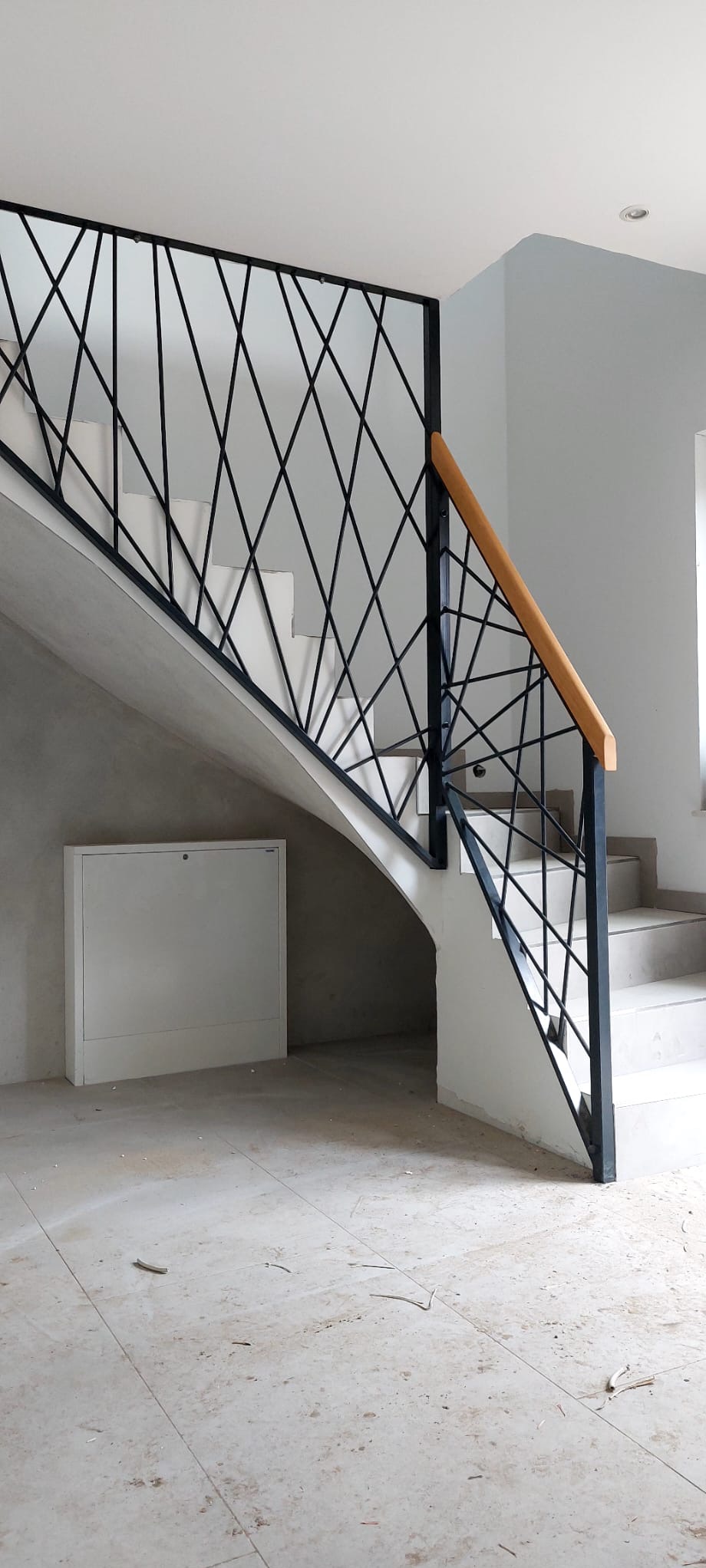 Nowoczesne schody z czarną, geometryczną balustradą i drewnianym poręczą. Widok z dołu, ukazujący detale konstrukcji i wykończenia. Minimalistyczny design.