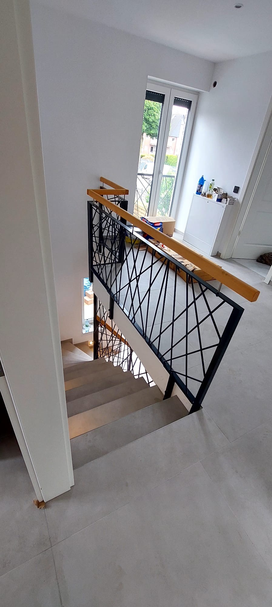 Nowoczesne schody z metalową balustradą o geometrycznym wzorze, drewniane poręcze, widok z góry, jasne wnętrze z oknem. Minimalistyczny design.