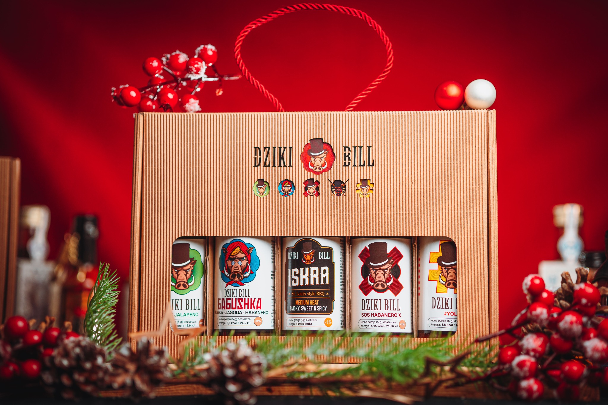 Zestaw prezentowy Dziki Bill: pięć sosów w ozdobnym kartonowym pudełku z motywem świątecznym na czerwonym tle. Idealne na prezent dla smakosza ostrych smaków.
