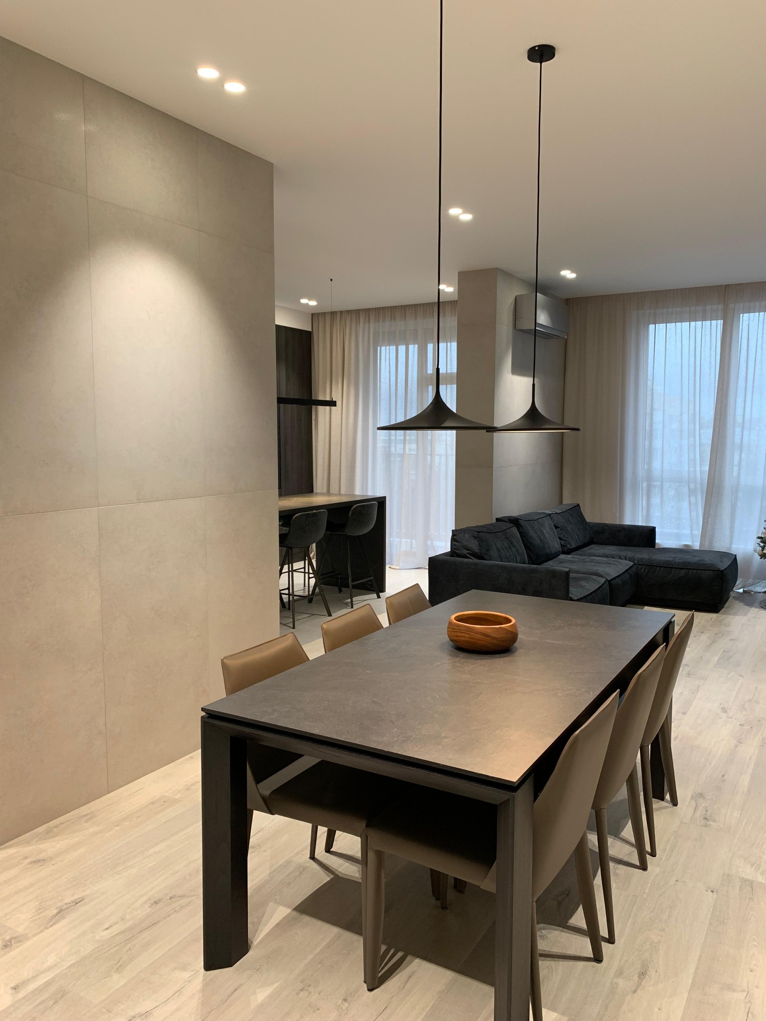 Nowoczesne wnętrze: stół z krzesłami, sofa i oświetlenie w minimalistycznym stylu. Jasne podłogi i ściany tworzą przestronny klimat. Widoczne detale wykończenia.