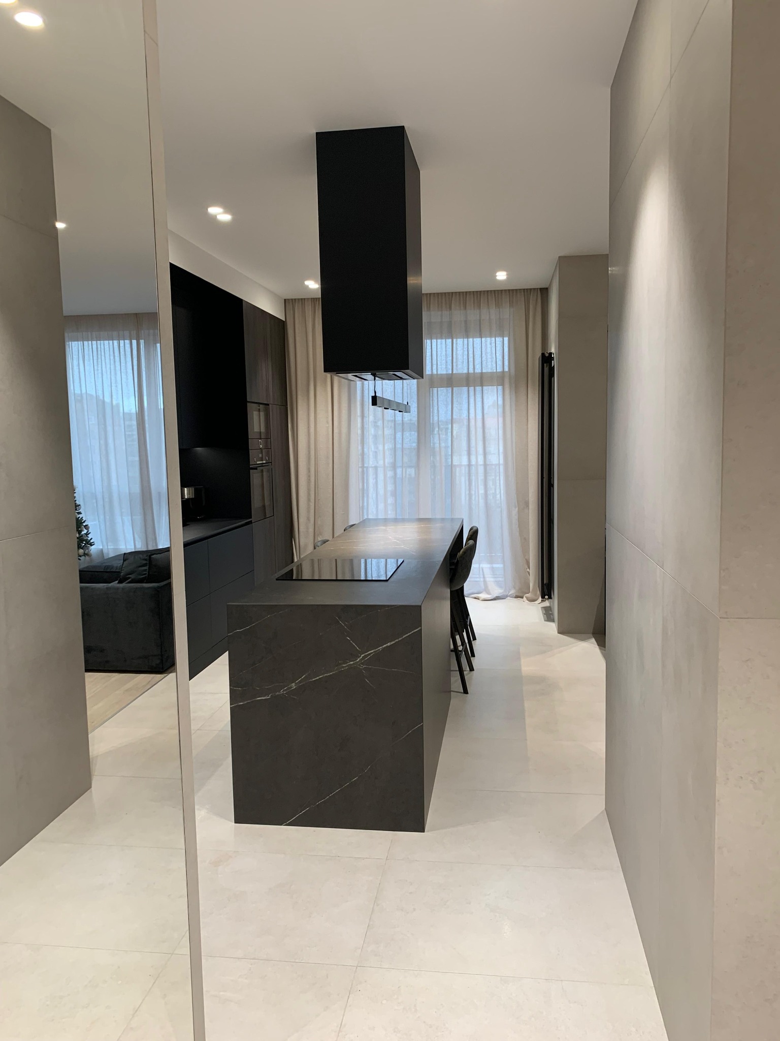 Nowoczesna kuchnia z wyspą w odcieniach szarości i czerni, minimalistyczny design, jasne płytki podłogowe, widok z perspektywy lustra, subtelne oświetlenie.