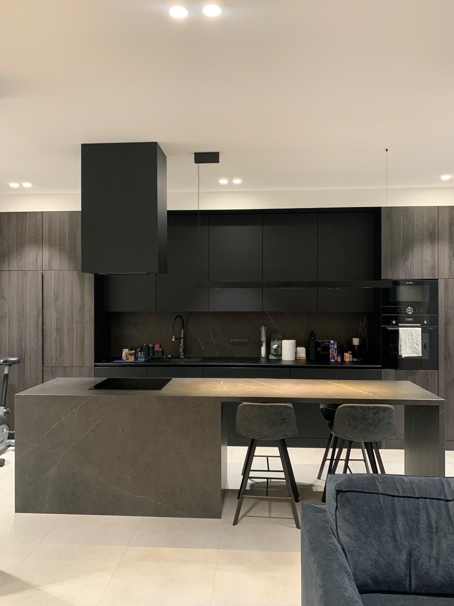 Nowoczesna kuchnia w odcieniach szarości i czerni. Wyspa kuchenna z kamiennym blatem, minimalistyczne krzesła barowe, zabudowa kuchenna z piekarnikiem Bosch.