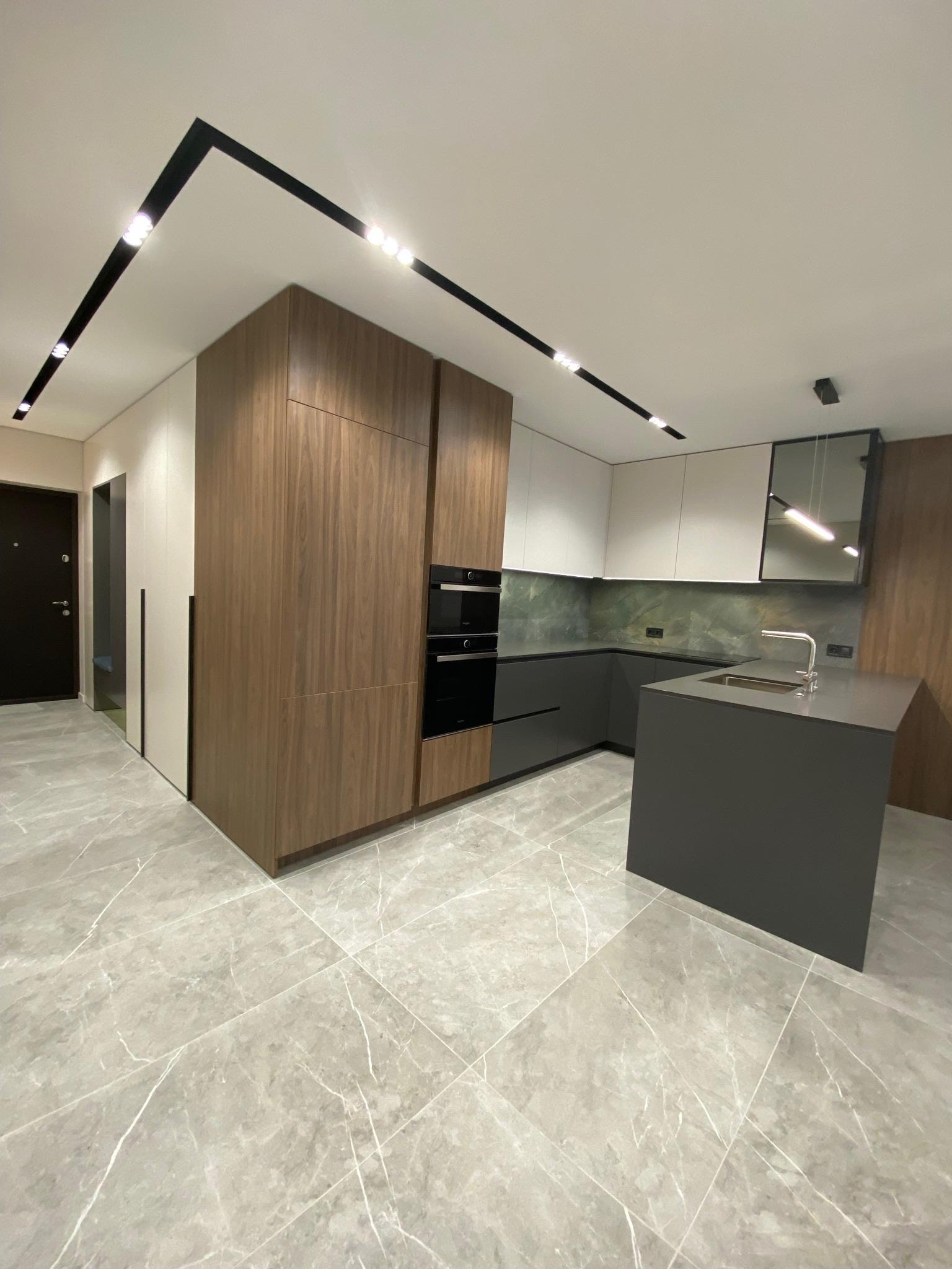 Nowoczesna kuchnia z wyspą, drewnianymi i białymi szafkami, marmurową podłogą i oświetleniem punktowym. Minimalistyczny design, eleganckie wykończenie.