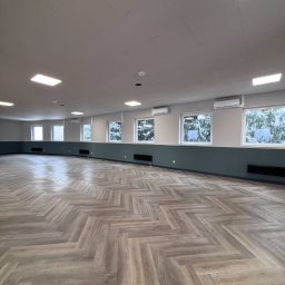 CHARUTA CHŁODNICTWO Bartosz Charuta - Jasne, przestronne wnętrze z parkietem w jodełkę, klimatyzatorami pod oknami i ciemnozieloną lamperią. Widok na zasypany śniegiem krajobraz za oknami.