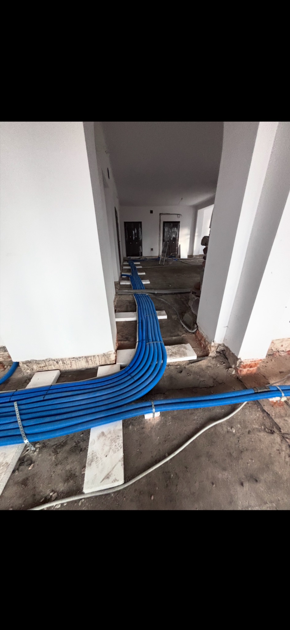 Niebieskie rury wentylacyjne ułożone równolegle na białych podkładkach w surowym wnętrzu. Widoczne fragmenty ścian i podłoża w trakcie prac instalacyjnych.