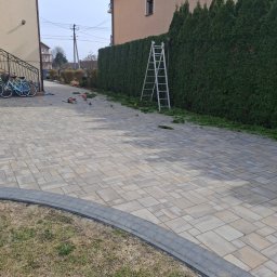 Usługi Ogrodnicze Ireneusz Góra - Przycięty żywopłot z tui, drabina oparta o rośliny, na kostce brukowej leżą obcięte gałązki i narzędzia ogrodnicze. Dwa rowery zaparkowane obok schodów.
