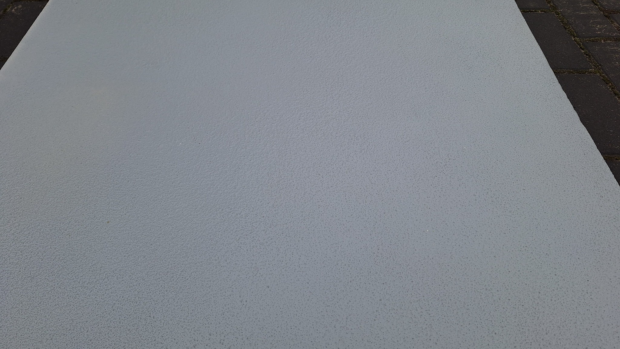 Jasnoszara, gładka powierzchnia z delikatną fakturą, prawdopodobnie wylana na zewnątrz, przylegająca do ciemnej kostki brukowej. Minimalistyczny kadr.