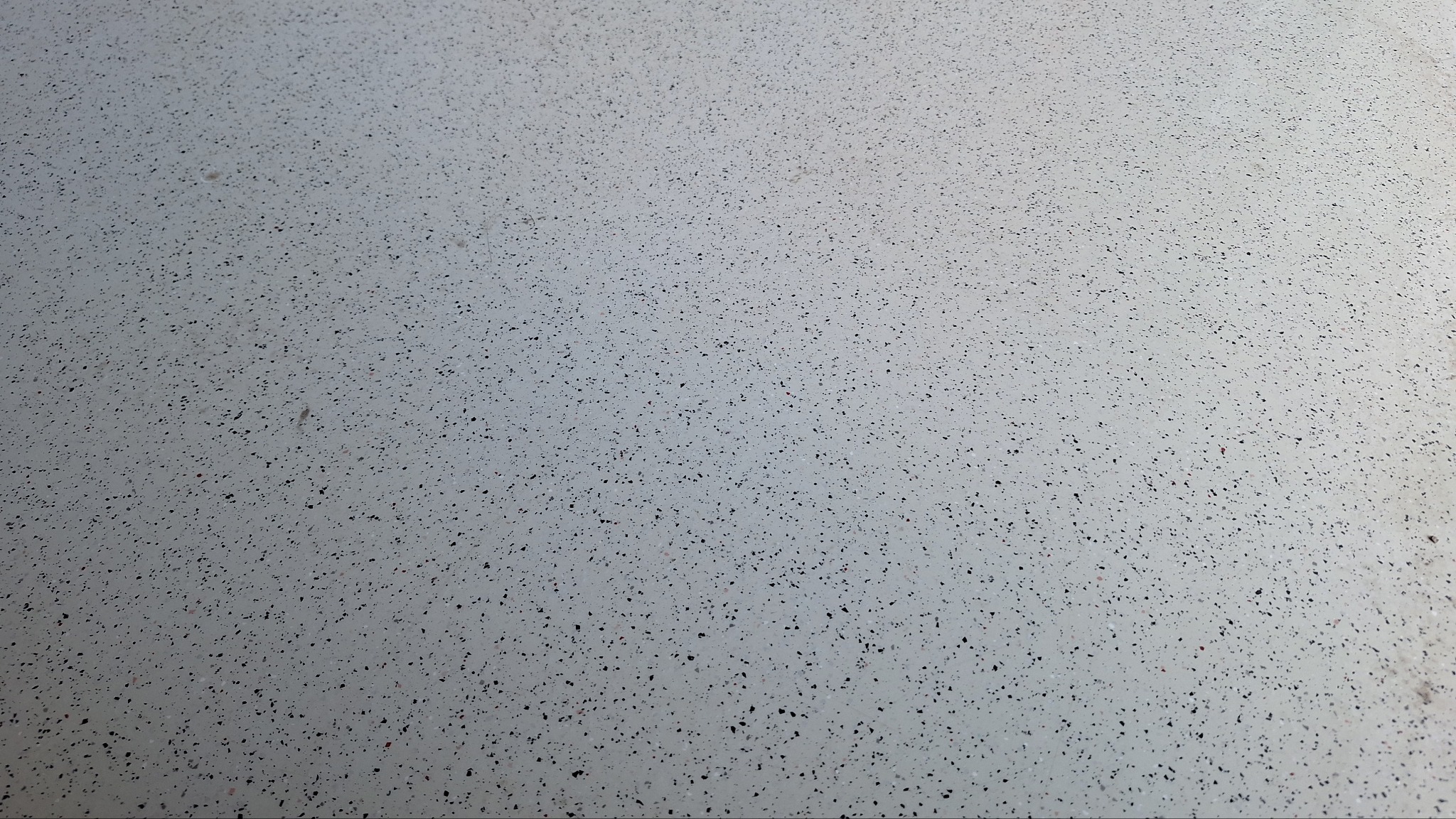 Jasnoszara, gładka powierzchnia z drobnymi, ciemnymi plamkami, tworząca jednolitą strukturę. Minimalistyczny wzór, równomierne rozłożenie elementów.