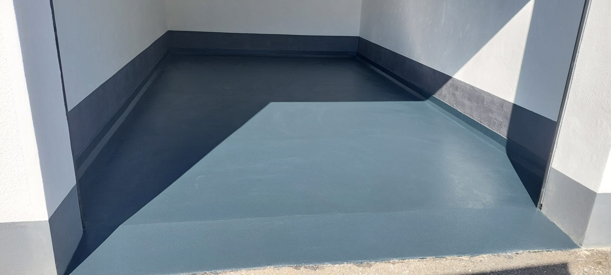 Gładka, szara posadzka żywiczna w garażu lub pomieszczeniu gospodarczym, z widocznym cieniem i wykończonymi na szaro ścianami.