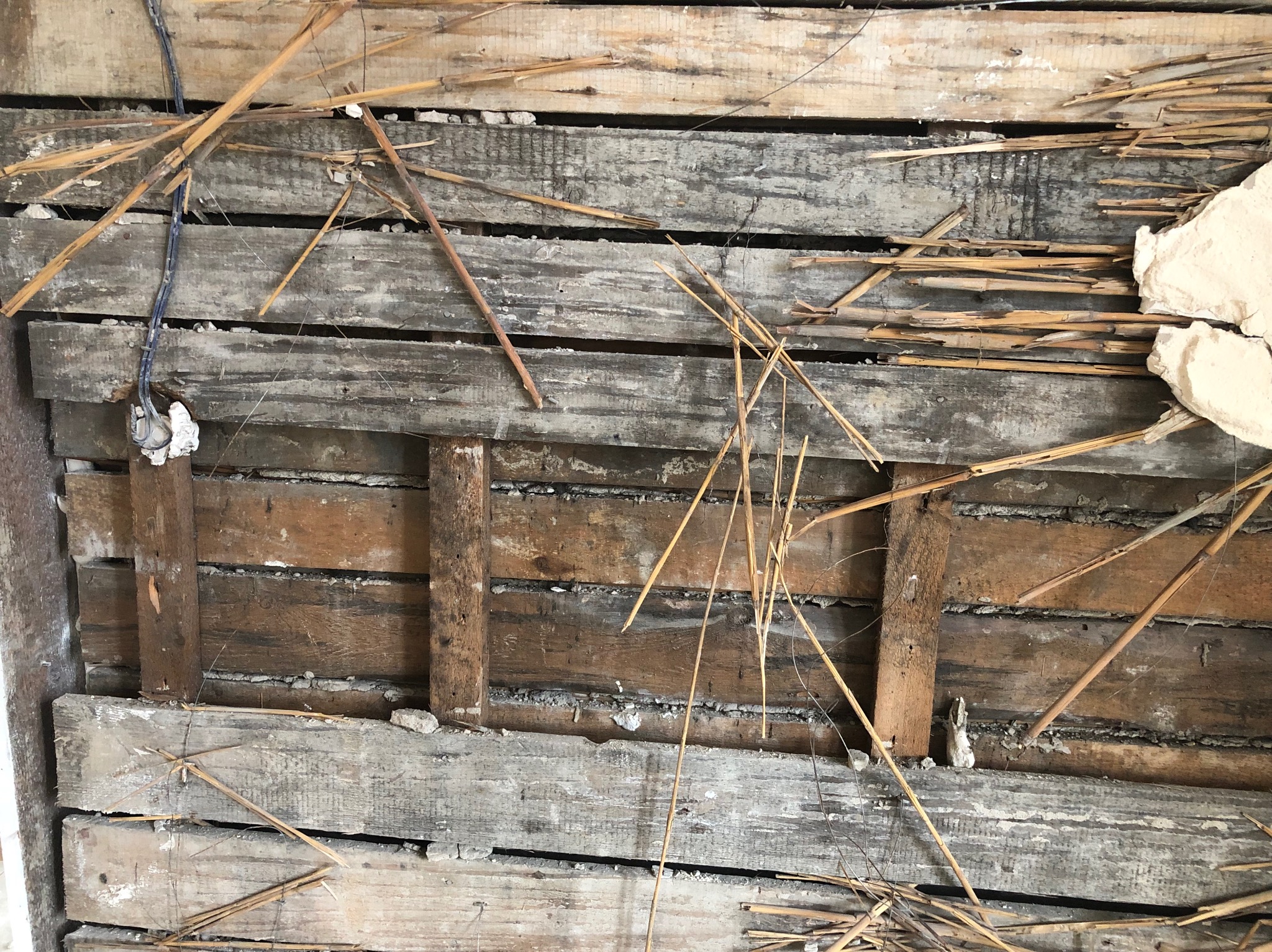 Fragment drewnianej ściany z widocznymi elementami konstrukcyjnymi i resztkami materiałów budowlanych, ukazujący etap prac rozbiórkowych.