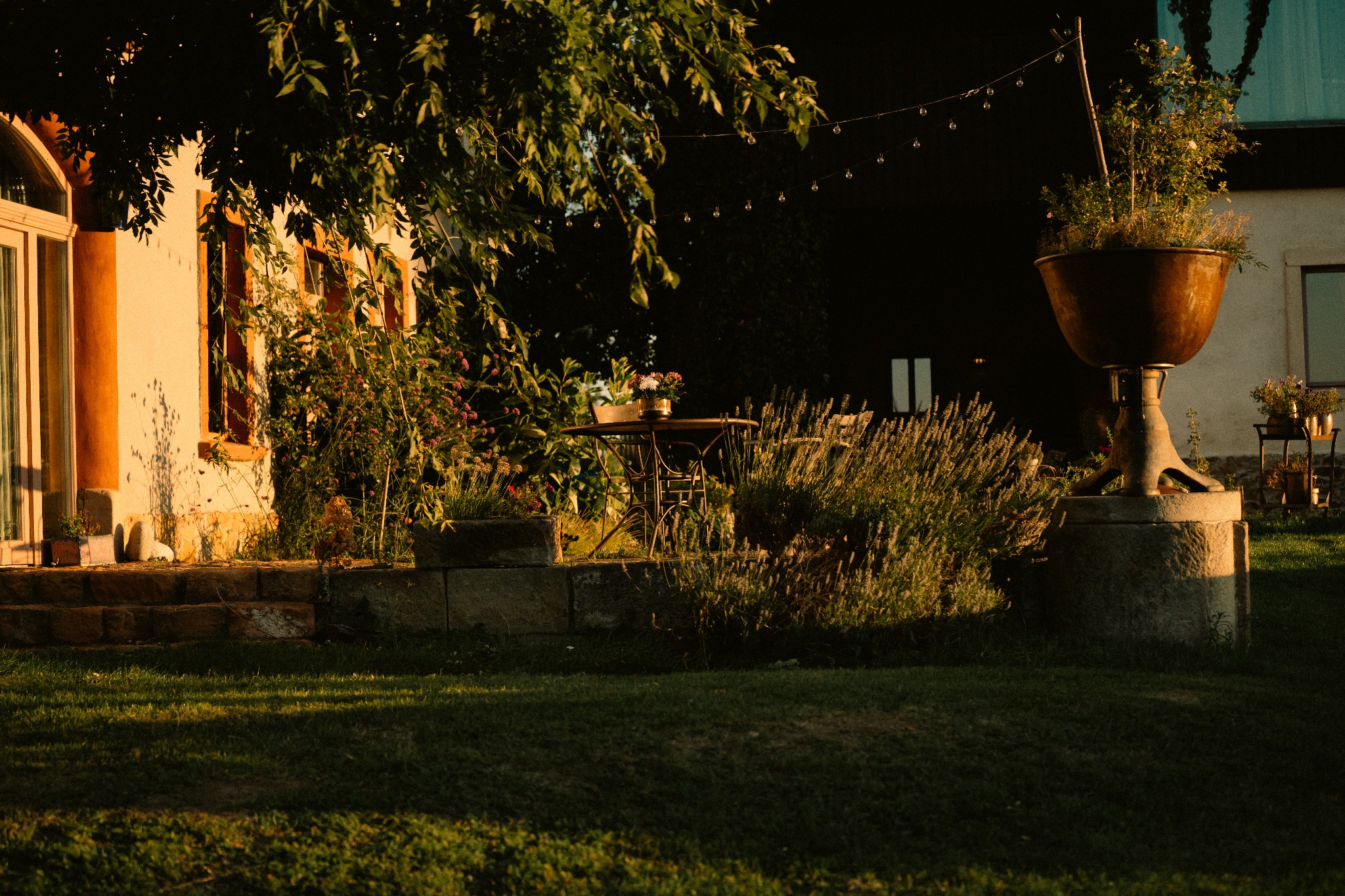 Urokliwy ogród z kamiennymi schodami, stolikiem kawowym i dekoracyjną donicą na postumencie, oświetlony ciepłym, popołudniowym światłem. Romantyczna atmosfera.