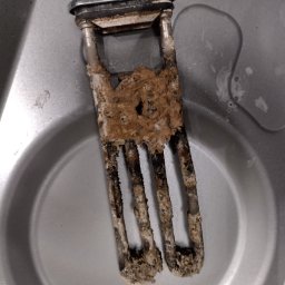 KK SERWIS KAMIL KOCYŁA - Zdemontowana, silnie zakamieniona grzałka z pralki, widoczne osady wapienne i korozja, leżąca w metalowej misce. Detal z bliska, ukazujący stopień zużycia elementu.