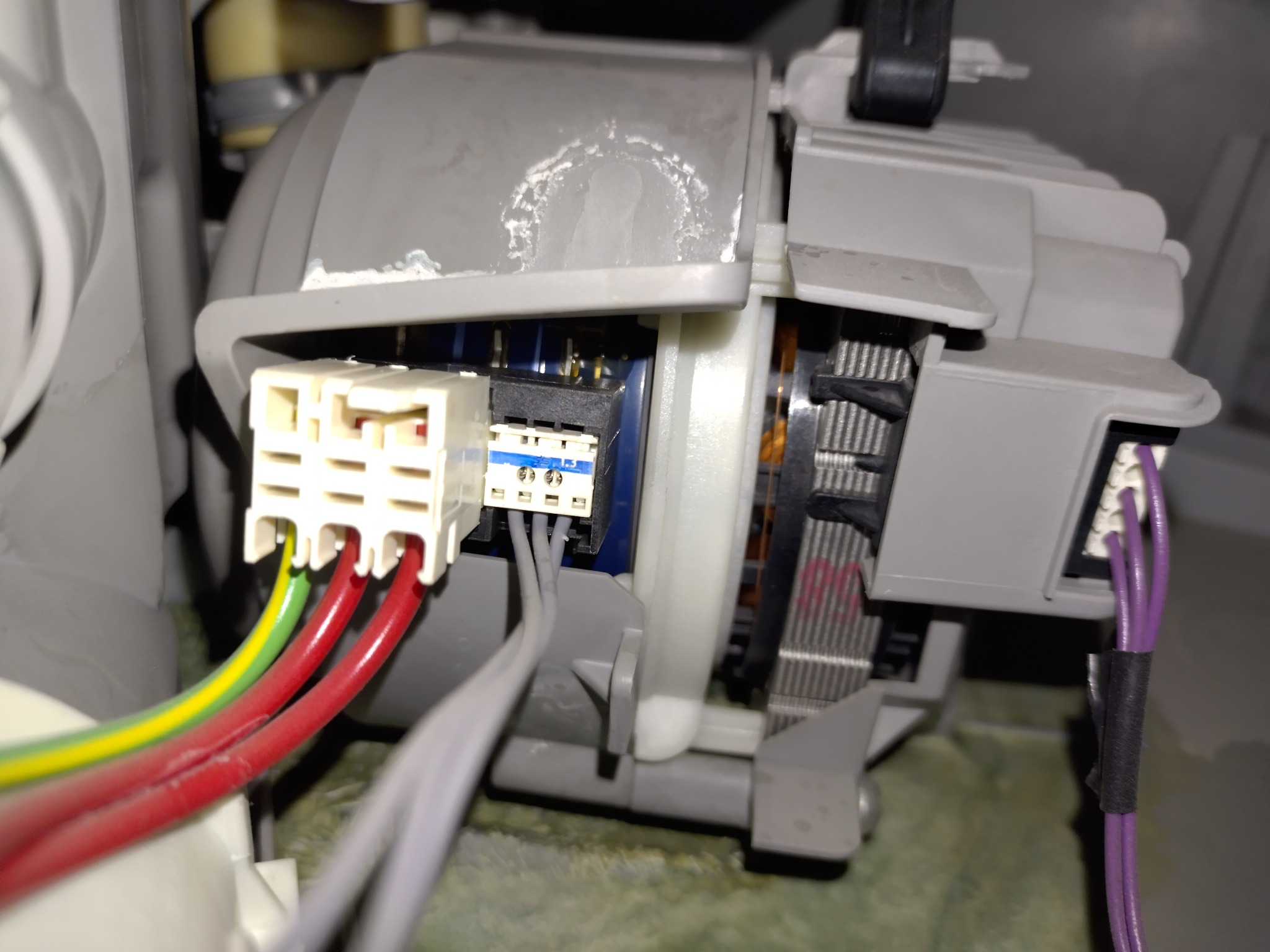 Wnętrze pralki z widocznym silnikiem, okablowaniem i złączkami. Detal naprawy lub serwisu AGD, z bliska ukazujący podłączenie przewodów.