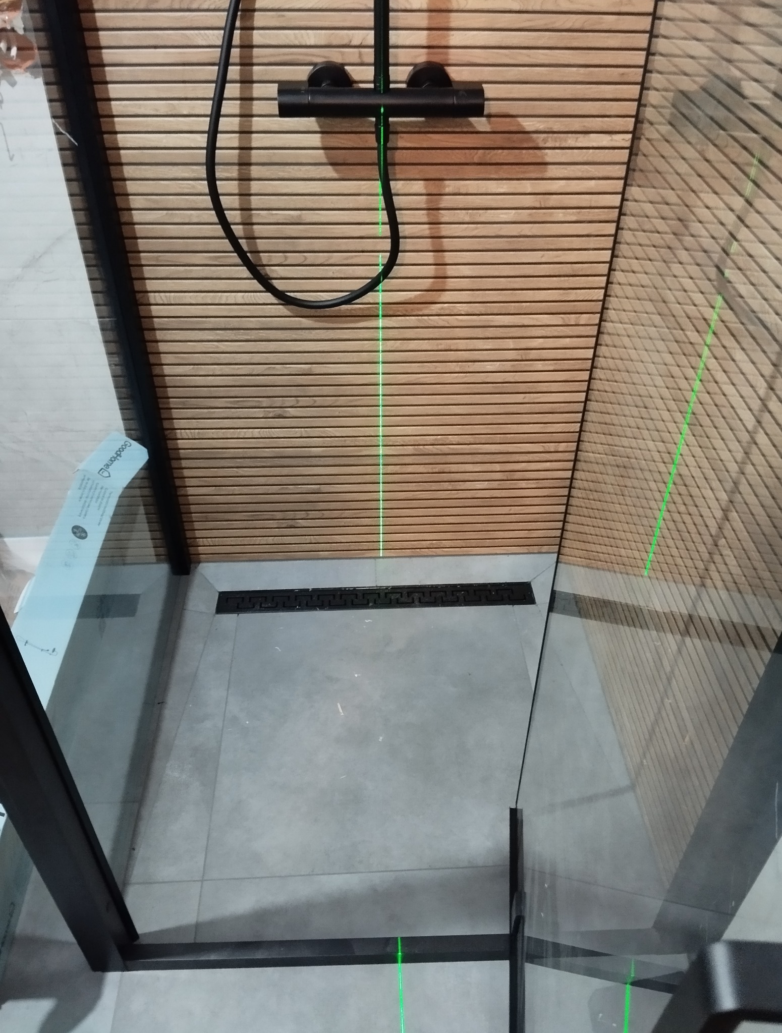 Nowoczesna kabina prysznicowa z drewnianą okładziną ścienną i czarną armaturą, poziomowana laserowo. Minimalistyczny design z odpływem liniowym.