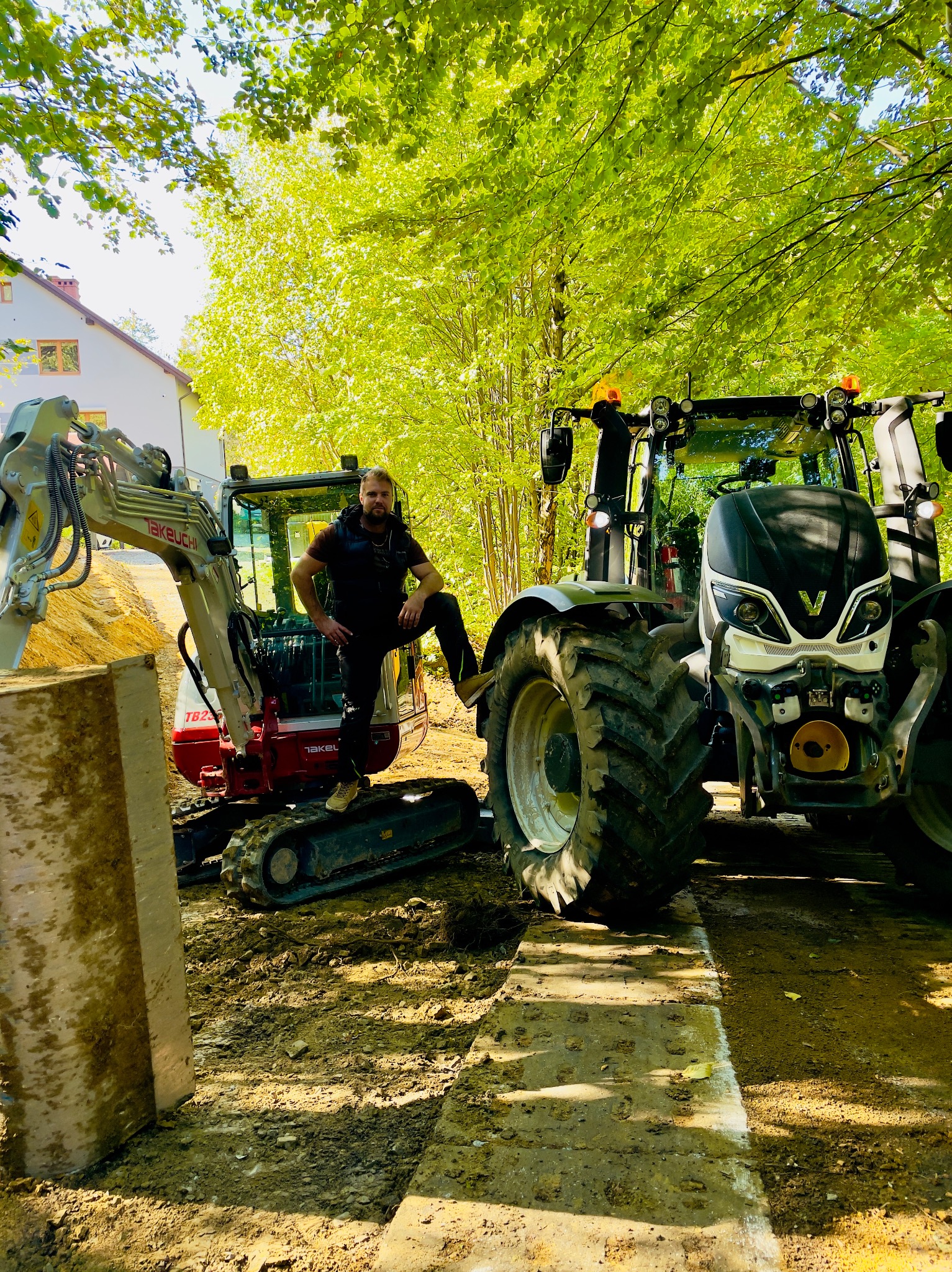 Operator na minikoparce Takeuchi TB225 obok traktora Valtra w Brennej. Sprzęt gotowy do prac ziemnych na tle zieleni.