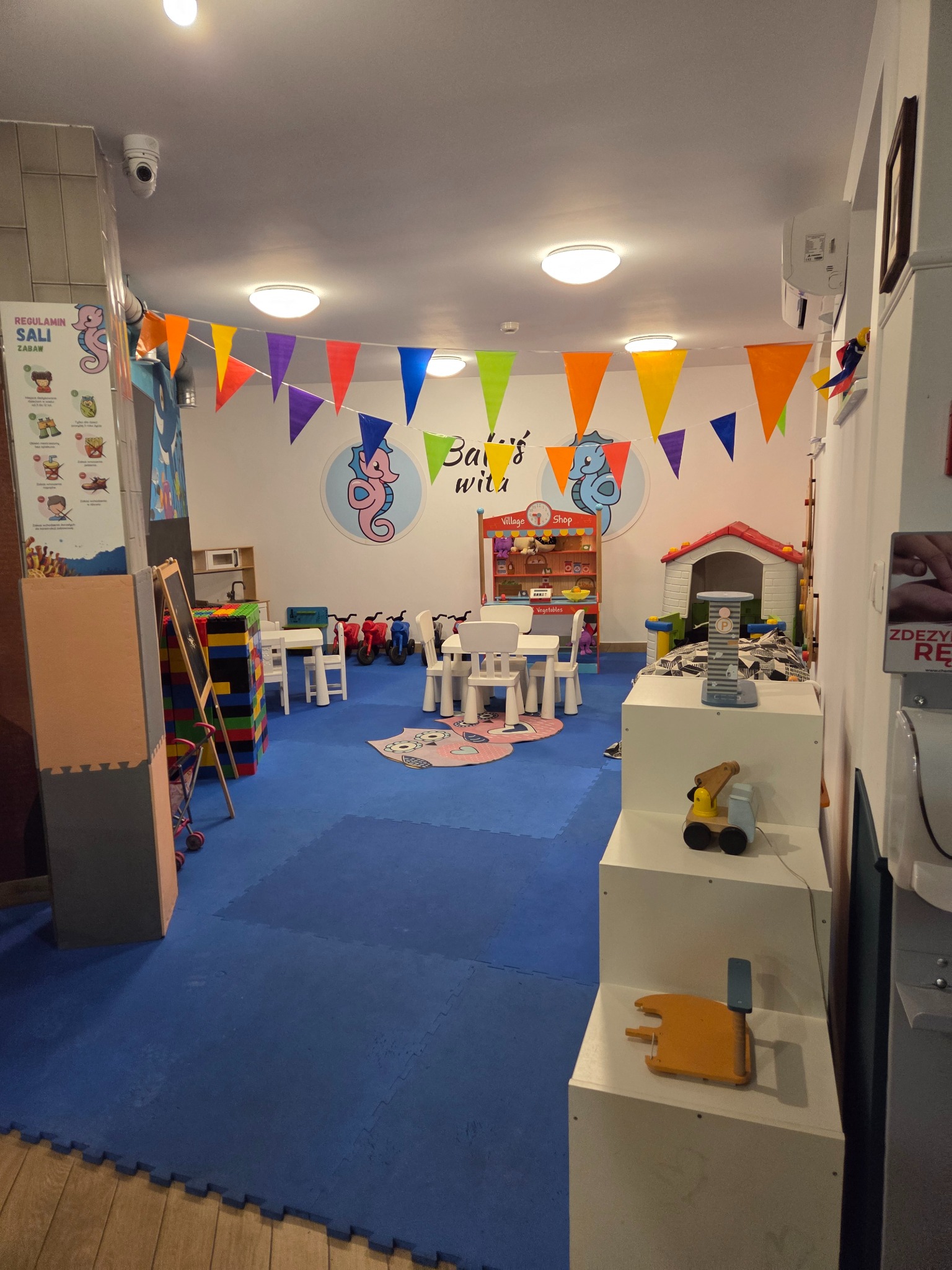 Kolorowa sala zabaw dla dzieci z dekoracjami, zabawkami i meblami, idealna na imprezy urodzinowe i inne wydarzenia. Niebieska podłoga z puzzli.