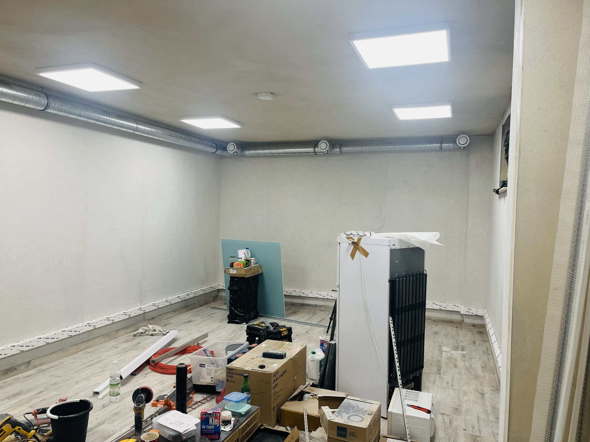 Wnętrze w trakcie prac wykończeniowych z zamontowanym oświetleniem sufitowym i widocznymi elementami wentylacji. Na podłodze narzędzia i materiały budowlane.