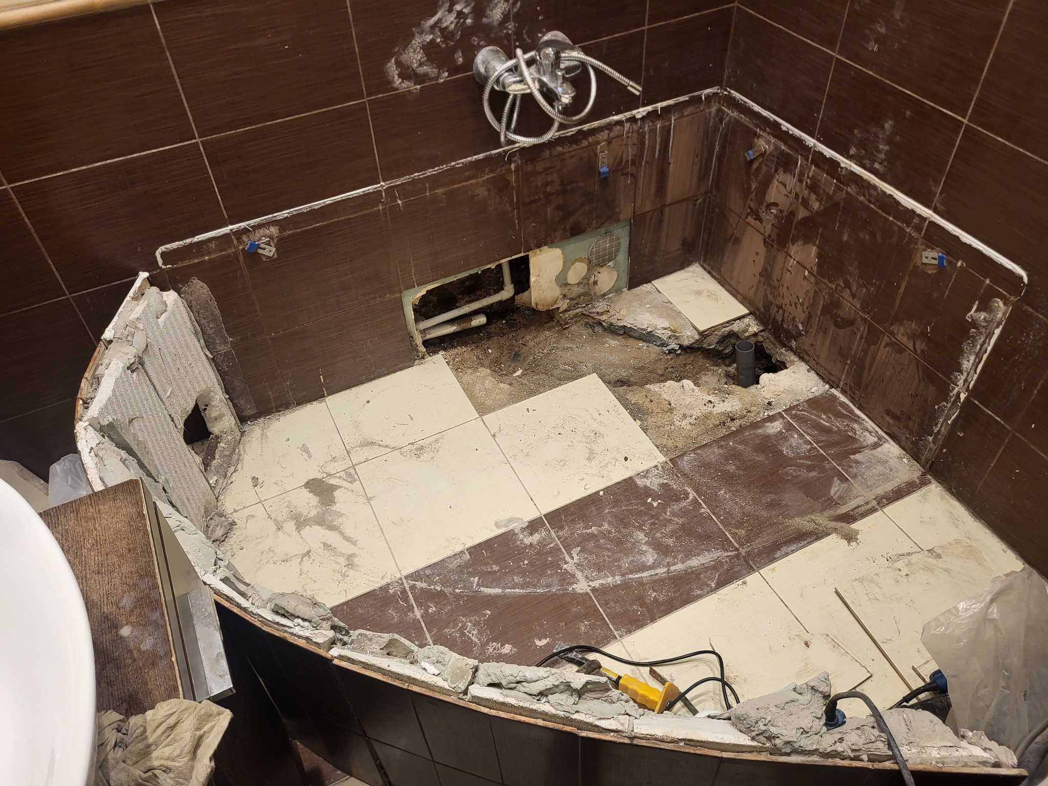 Demontaż płytek w łazience z widocznym odpływem i fragmentami instalacji. Użyte narzędzia sugerują etap prac przygotowawczych do remontu.