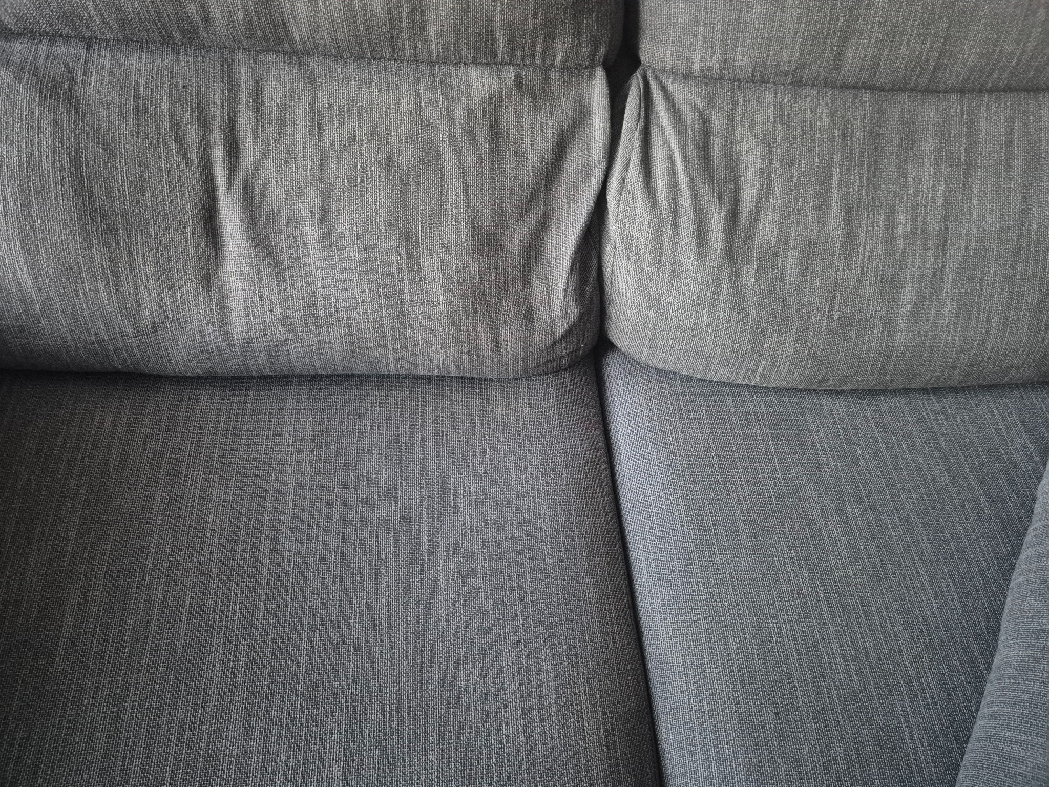 Szczegółowe ujęcie szarej, teksturowanej kanapy z widocznymi poduszkami i siedziskiem, ukazujące fakturę materiału i konstrukcję mebla.