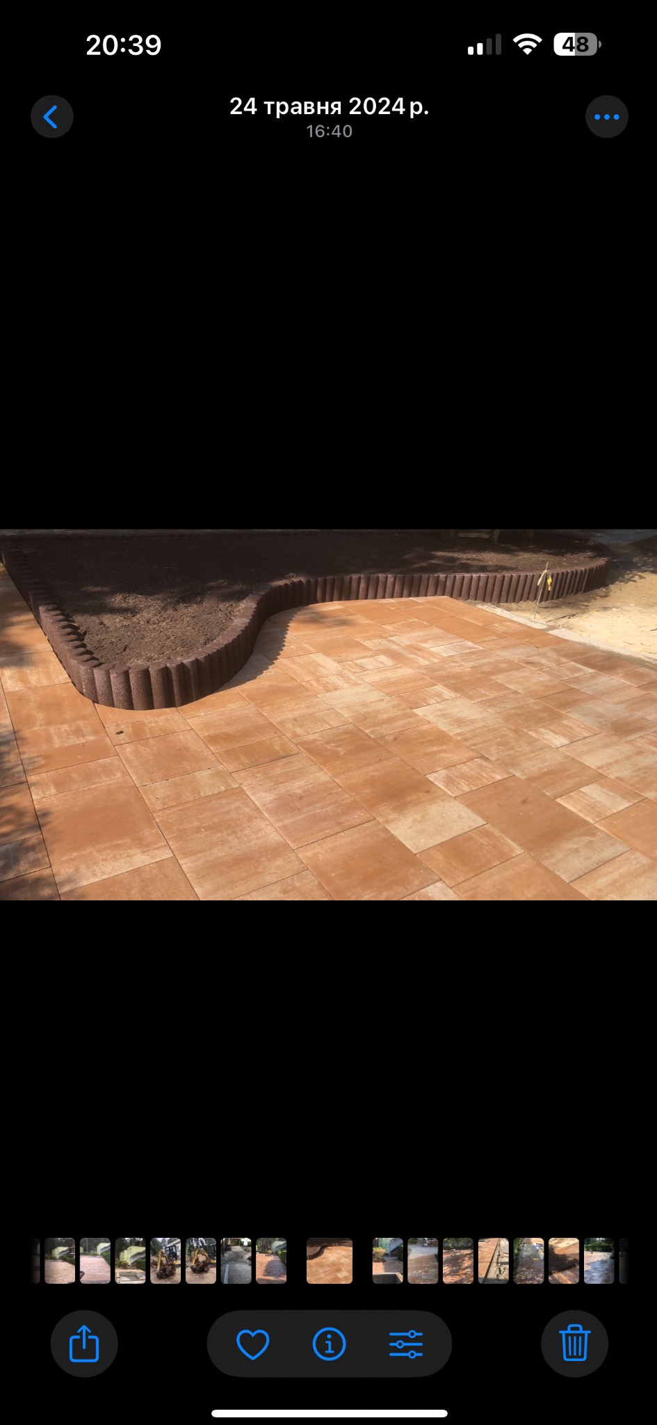 Ułożona, brązowa kostka brukowa tworząca ścieżkę, obrzeże z palisady oddziela ją od rabaty z ziemią. Widok z góry, słoneczny dzień.