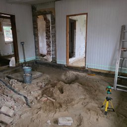 ART-BUD Artur Bomba - Wnętrze w trakcie remontu: wykopana podłoga, widoczne ślady po demontażu, poziomica laserowa, drabina oparta o ścianę. Prace przygotowawcze do dalszych etapów.