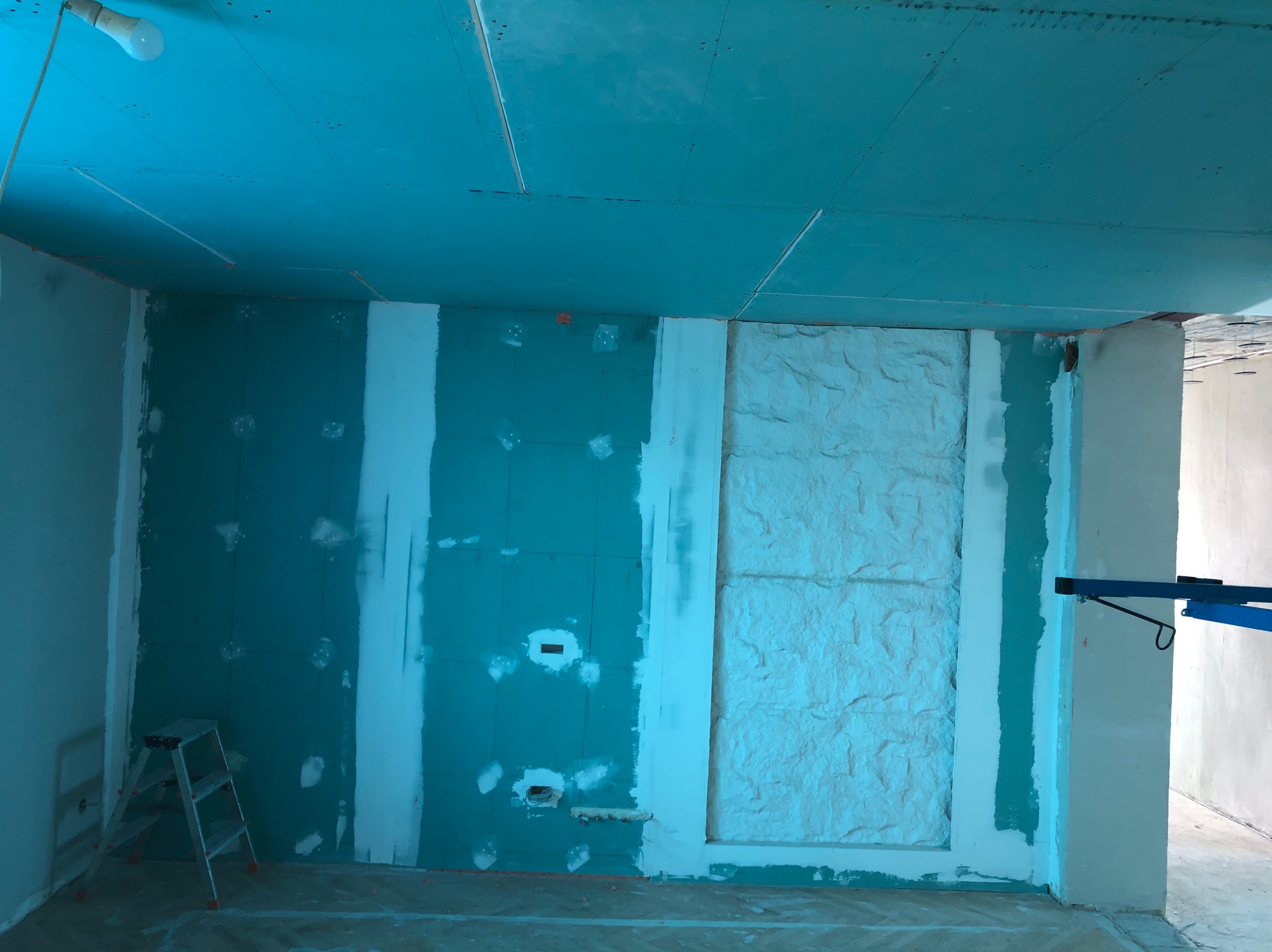 Wnętrze w trakcie prac wykończeniowych: ściany z płyt gipsowo-kartonowych, częściowo wyszpachlowane, sufit podwieszany, drabina malarska w rogu pomieszczenia.