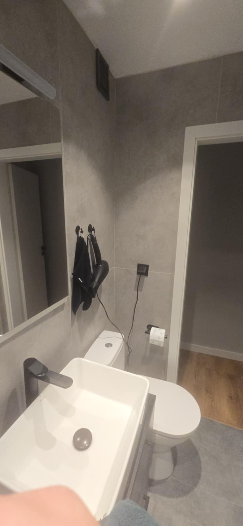 Nowoczesna łazienka w szarościach: umywalka nablatowa, toaleta, lustro i akcesoria. Minimalistyczny design z dbałością o detale, widoczne gniazdko elektryczne.