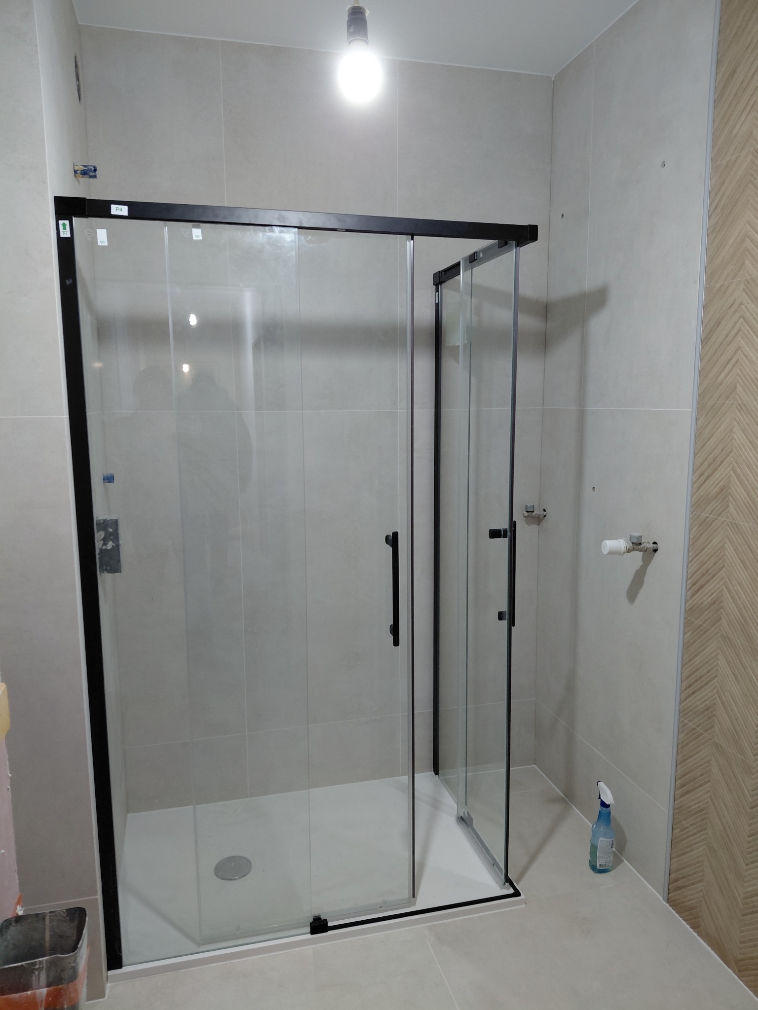 Nowoczesna kabina prysznicowa z czarnymi profilami i przesuwnymi drzwiami, zamontowana w jasnej łazience z beżowymi płytkami i dekoracyjną ścianą.