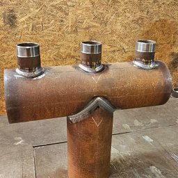 MAR-WELD Marcin Przybyszewski - Spawana konstrukcja rurowa z trzema króćcami, wykonana z metalu o rdzawym odcieniu, na tle płyty OSB. Widoczne spoiny i ślady obróbki.