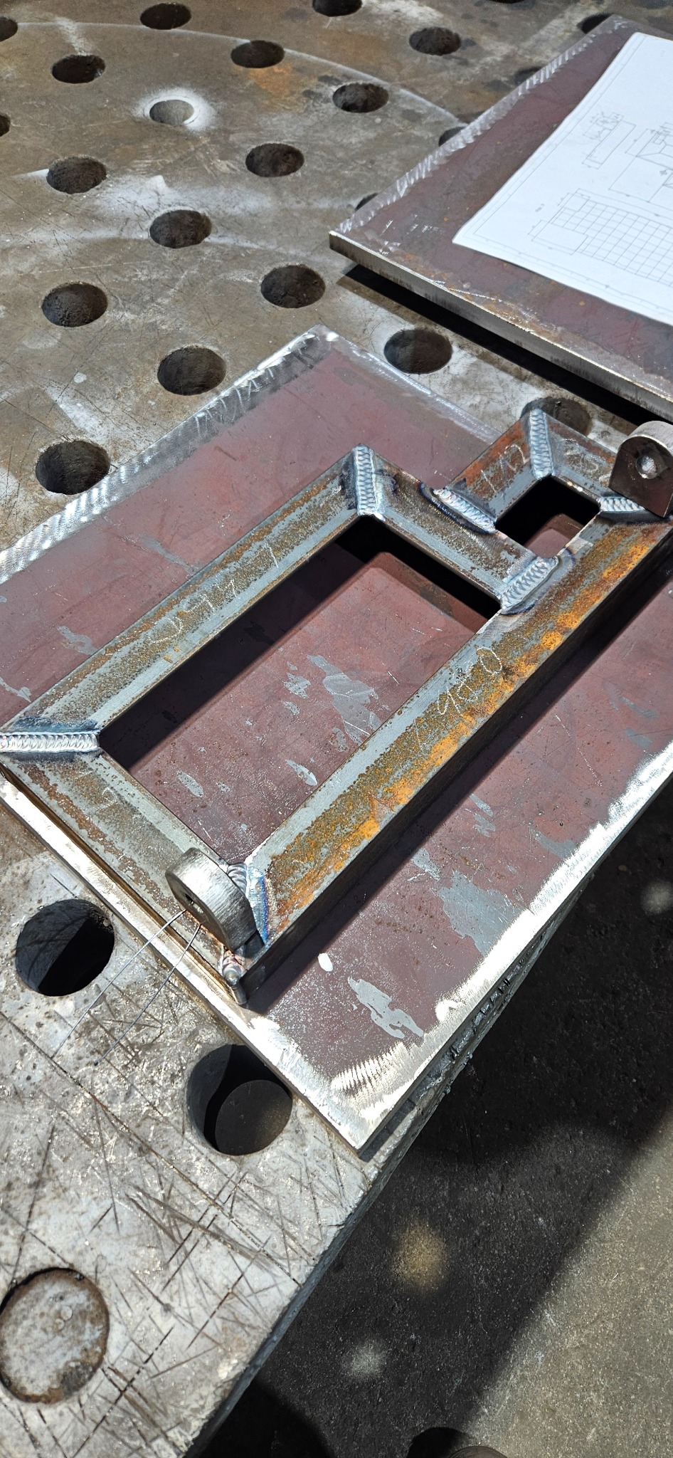 Metalowa konstrukcja spawana na stole spawalniczym w Tczewie. Widoczne spawy i elementy konstrukcyjne. Na stole leży rysunek techniczny.