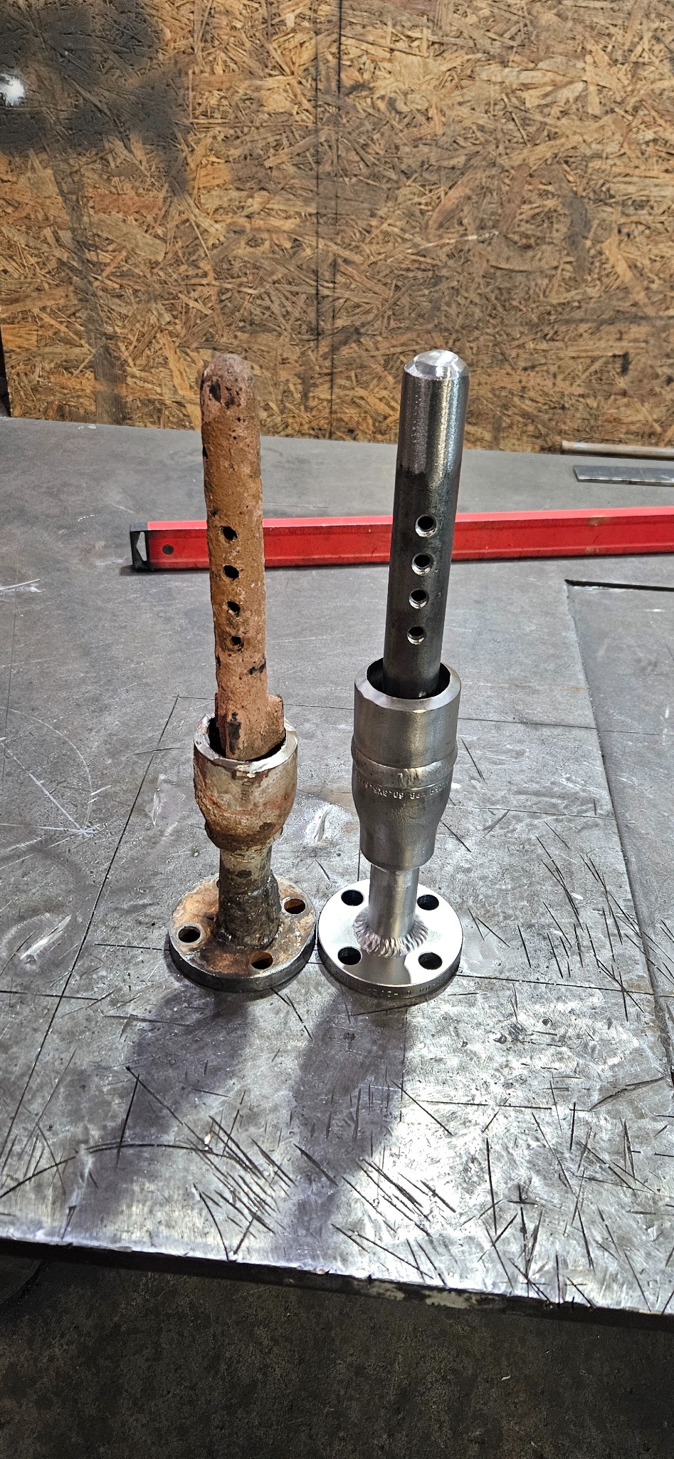 Porównanie: zardzewiały i odnowiony metalowy element z kołnierzem i otworami, leżące na metalowym stole warsztatowym. Widoczny czerwony poziomica w tle.