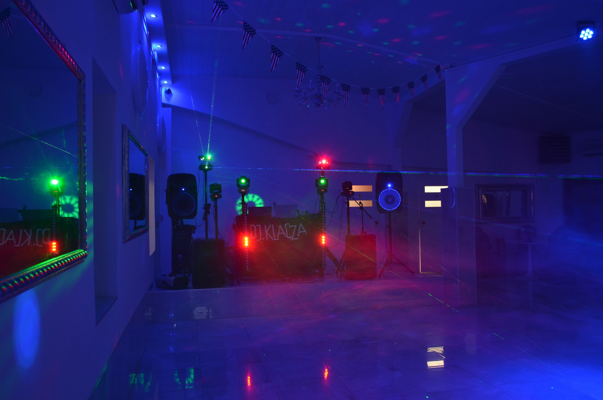 Sala z nagłośnieniem i oświetleniem DJ'a, dekoracje w postaci flag USA, lustra na ścianach, parkiet odbijający światła. Scena gotowa na imprezę.