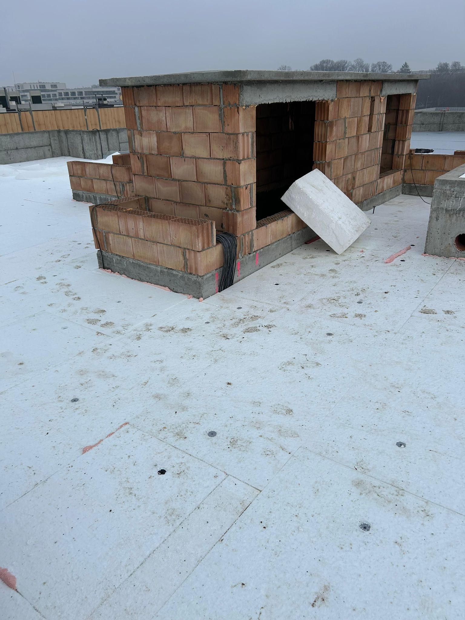 Budowa dachu płaskiego z cegły ceramicznej porotherm, widoczne ocieplenie styropianem. Elementy konstrukcyjne w trakcie wznoszenia, surowy stan.