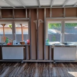 Michał Kliś - Wnętrze w trakcie prac wykończeniowych: widoczne profile pod płyty gipsowe, okna z grzejnikami, podłoga imitująca drewno. Częściowo zaszpachlowana ściana.