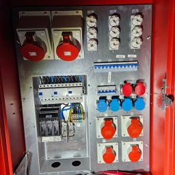GENERAL ELEKTRO Grzegorz Kaczor - Rozdzielnica elektryczna w czerwonej obudowie, widoczne bezpieczniki, gniazda siłowe (czerwone i niebieskie), listwy zaciskowe i narzędzia elektryczne na dnie szafy.