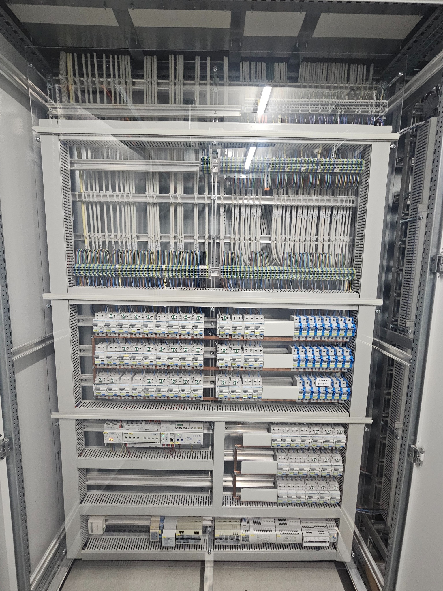 Rozdzielnica elektryczna z licznymi zabezpieczeniami, okablowaniem i listwami zaciskowymi, widoczna wewnątrz szafy sterowniczej. Precyzyjny montaż.