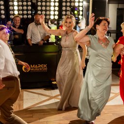 M&M EVENTS MAREK MURAWSKI - Roztańczona sala balowa z DJ-em w tle, oświetlenie punktowe, parkiet. Goście weselni w ruchu, w eleganckich strojach. Marek Murawski DJ & Prezenter.