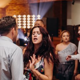 M&M EVENTS MAREK MURAWSKI - Wokalistka z ekspresją śpiewa podczas występu w Łapach, otoczona publicznością. W tle widoczne oświetlenie sceniczne, tworzące intymną atmosferę wydarzenia.