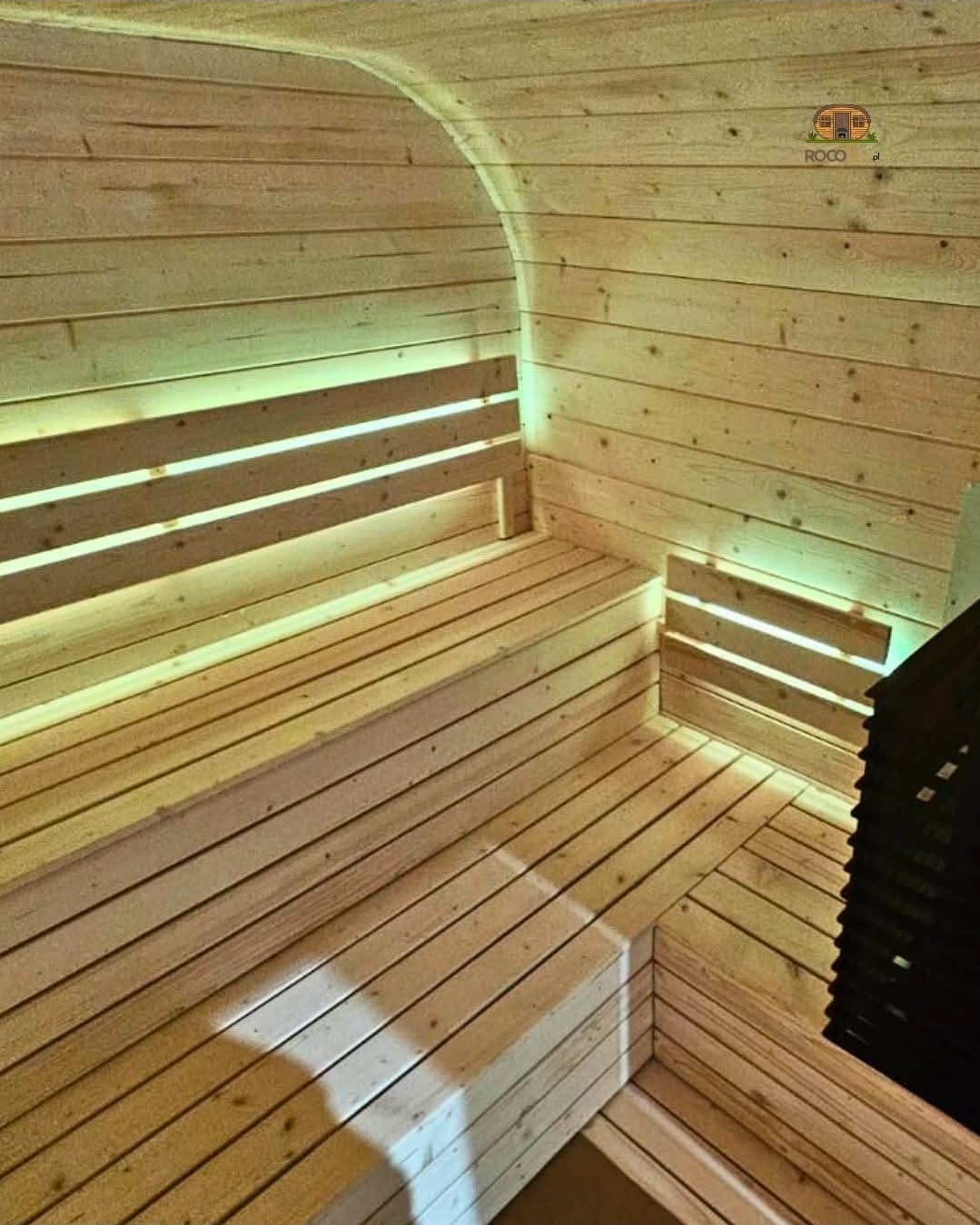 Wnętrze sauny beczki z podświetlanymi ławkami w Człuchowie. Drewniane wykończenie, ciepłe oświetlenie tworzy relaksującą atmosferę. Widok na piec.