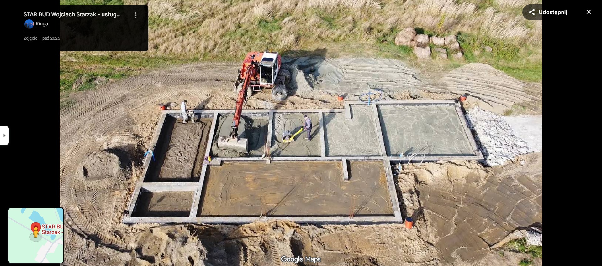 Z góry widok na fundamenty domu w trakcie budowy. Koparka w wykopie, pracownicy zagęszczają podłoże. Widoczne szalunki i przygotowane podłoże pod wylewkę.
