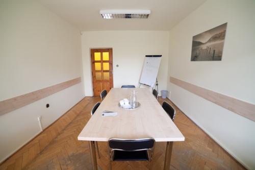 Jasna sala konferencyjna z drewnianym stołem, krzesłami, flipchartem i grafiką na ścianie, przygotowana do spotkania.