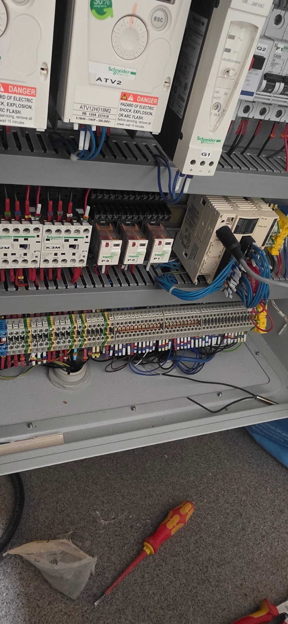 Rozdzielnica elektryczna z widocznymi elementami sterowania, zabezpieczeniami i okablowaniem. Widoczne komponenty Schneider Electric i narzędzie - śrubokręt.