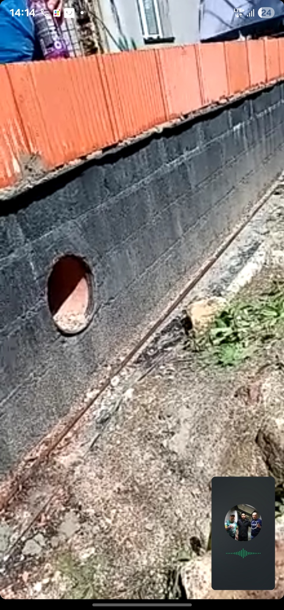 Ceglana ściana fundamentowa z otworem wentylacyjnym, pomalowana na czarno, z widoczną instalacją. Ujęcie z dołu, ukazujące detale konstrukcyjne i otoczenie.