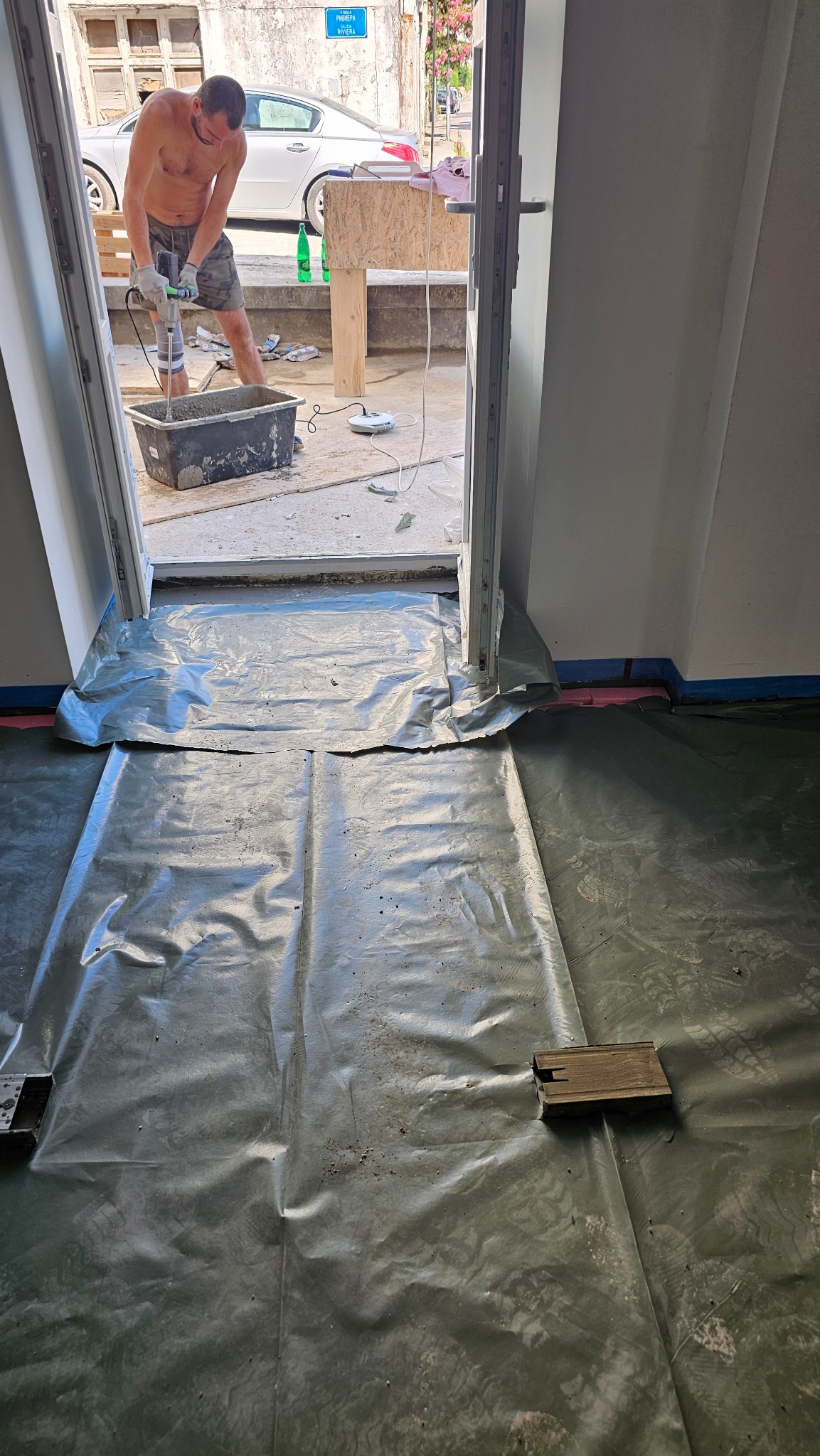 Przygotowanie podłoża pod wylewkę: folia ochronna na podłodze, widoczny pracownik mieszający zaprawę w wiadrze. Prace remontowe wewnątrz budynku.