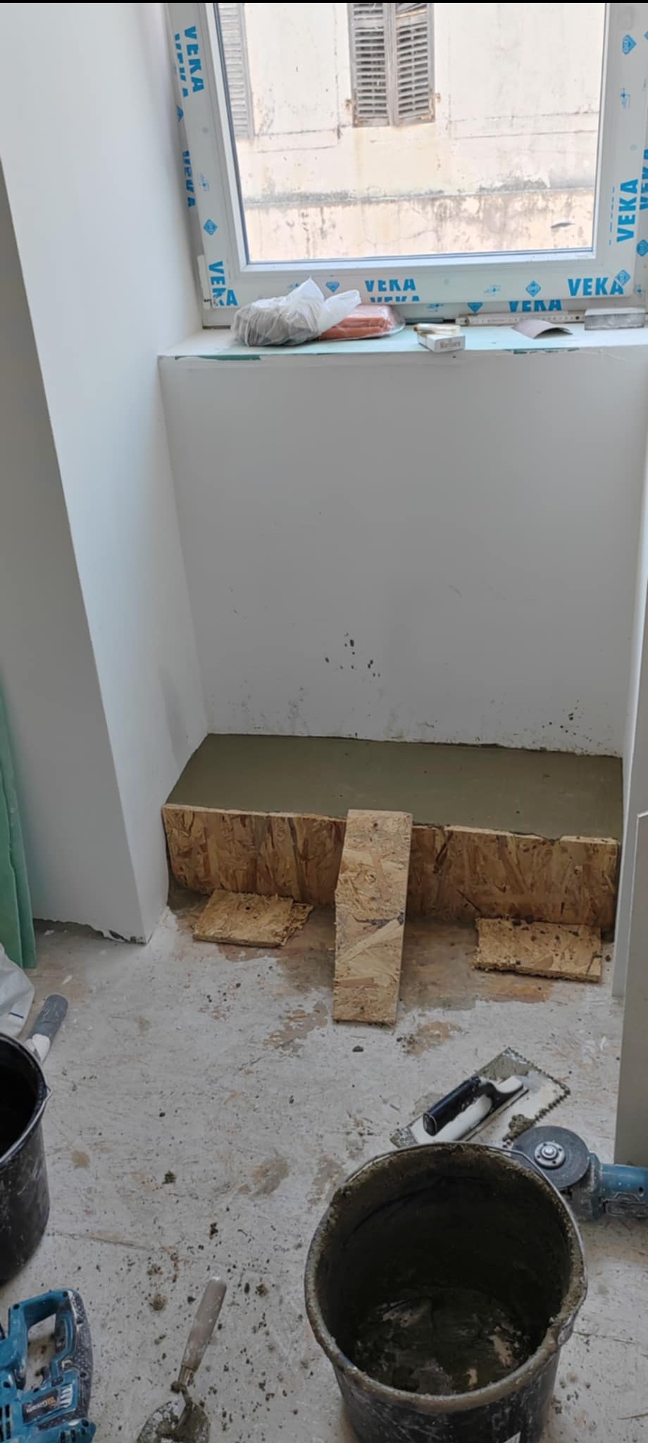 Wnętrze w trakcie prac remontowych: przygotowane podłoże z płyt OSB pod wylewkę, widoczne narzędzia i wiadro z zaprawą. Okno dachowe w tle.