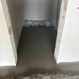 Posadzki Maszynowe - Posadzki Przemysłowe - ZAMBUD - Świeżo wylana, gładka posadzka w pomieszczeniu z widoczną siatką zbrojeniową w tle. Surowe ściany i widoczne ślady prac budowlanych.